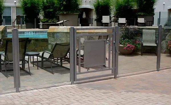 Pool area with gray metal fence, gate, chairs, and greenery.