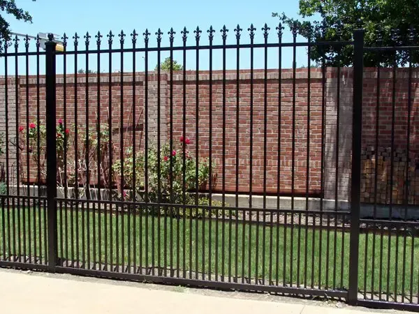 Black metal fence in front of a brick wall and green grass.