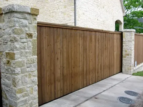 Wooden fence with stone pillars in front of a light-colored building.