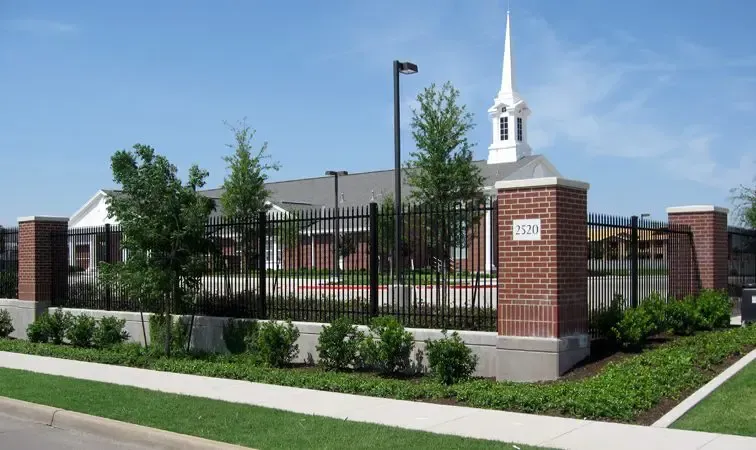 Church building behind a black fence, with a white steeple and red brick accents.