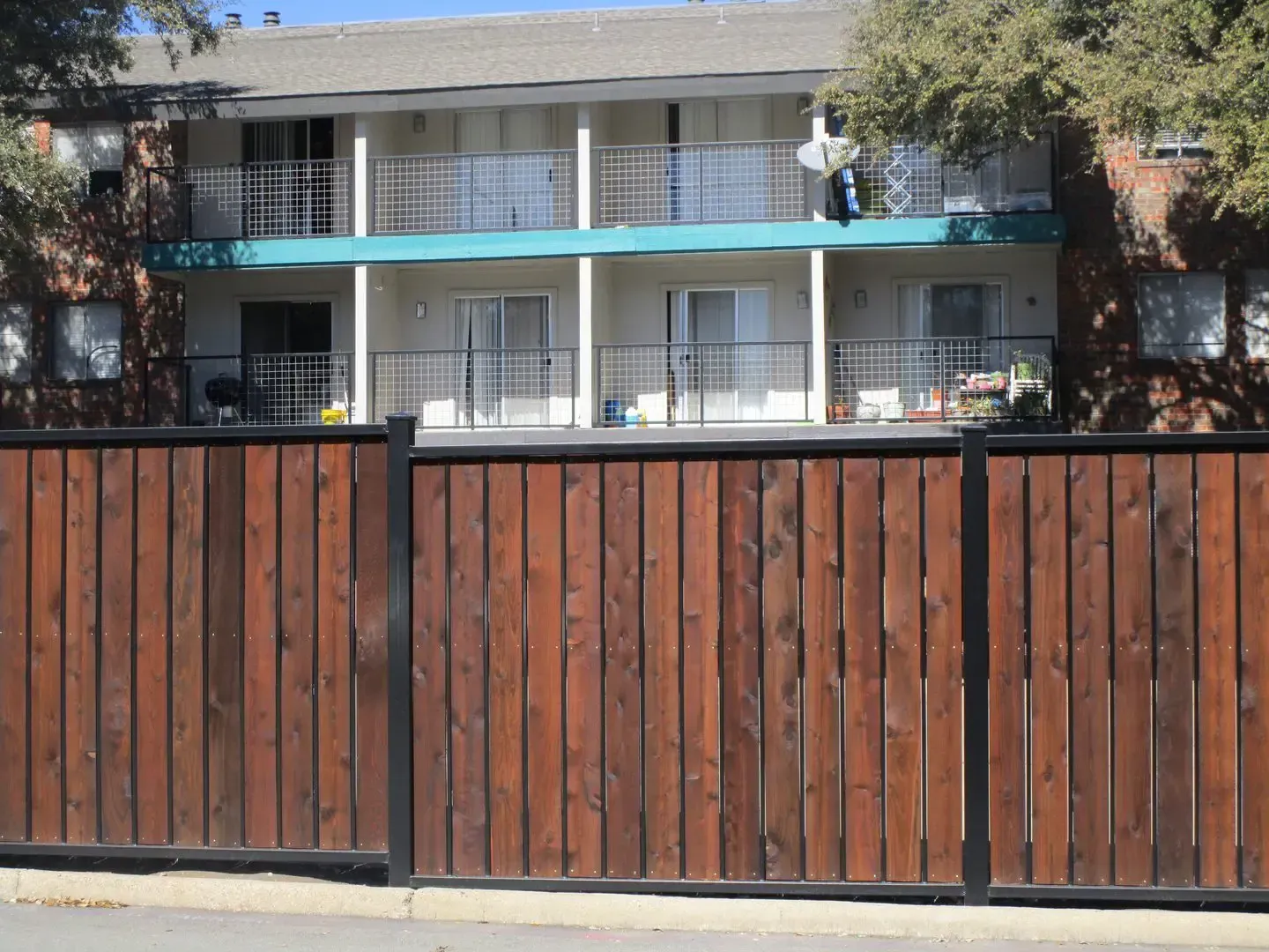 Brown wooden fence in front of a two-story apartment building with balconies.