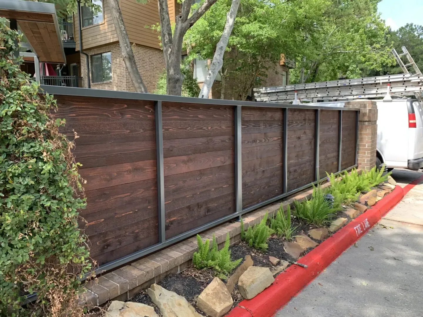 Modern wooden fence with metal frame and red curb alongside a building.