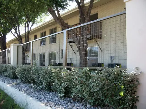 Apartment building exterior with metal fence, hedges, and gravel landscaping.