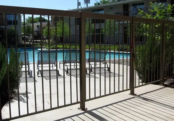 Bronze metal fence surrounding a pool area with chairs, on a sunny day.