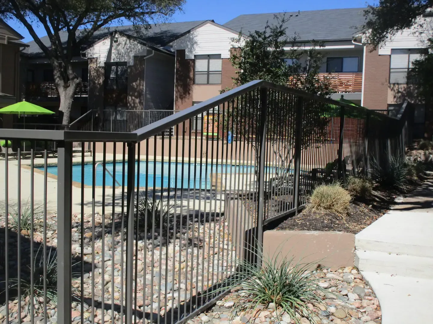 Pool area with dark metal fence, apartment building in the background.