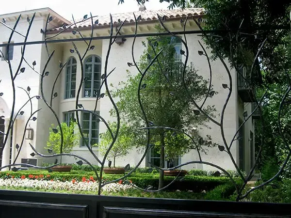 Decorative metal fence with a house and greenery in the background.