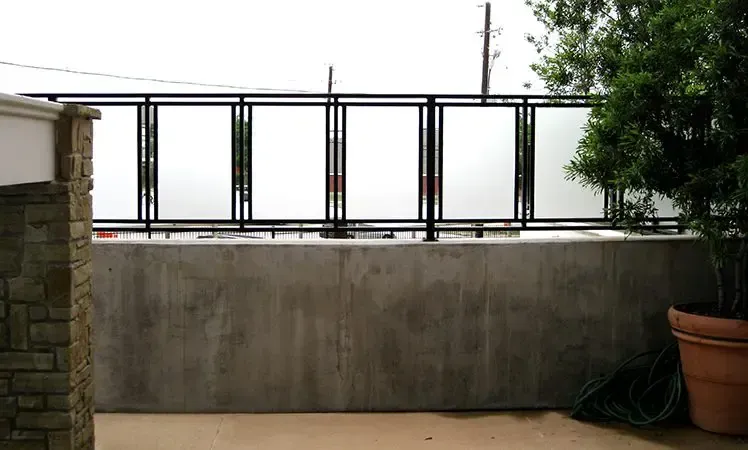 Black metal and frosted glass railing on concrete wall with potted plant.