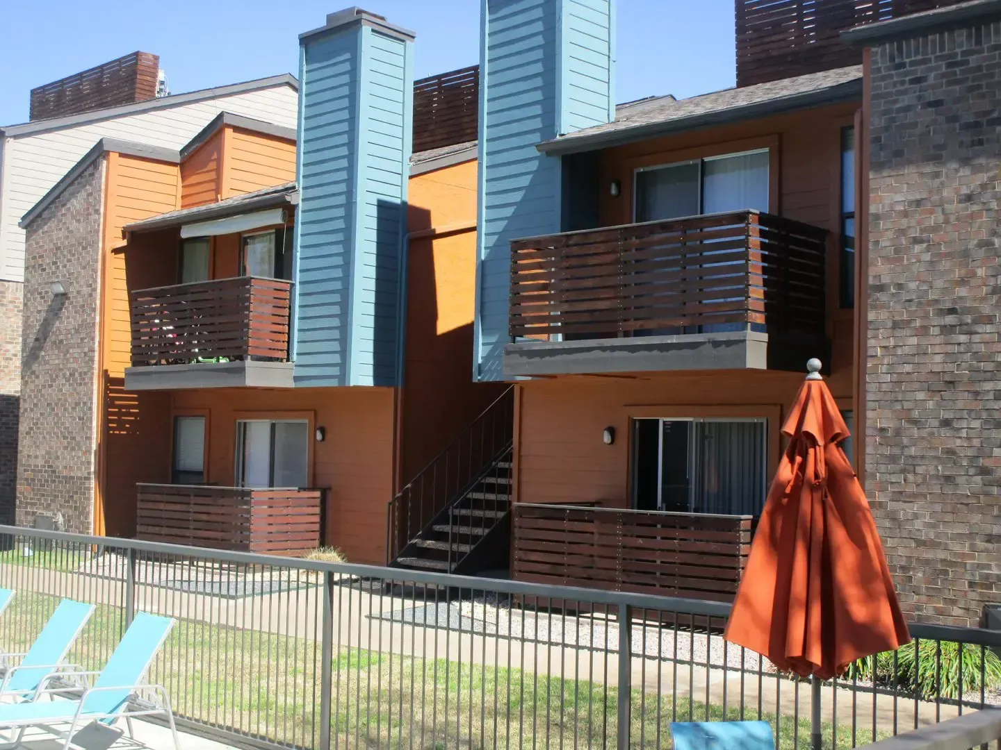 Apartment building with orange and blue accents, balconies, and pool with orange umbrella.