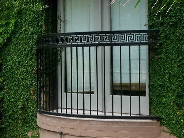Black wrought iron balcony with Greek key design railing against a green ivy-covered wall.
