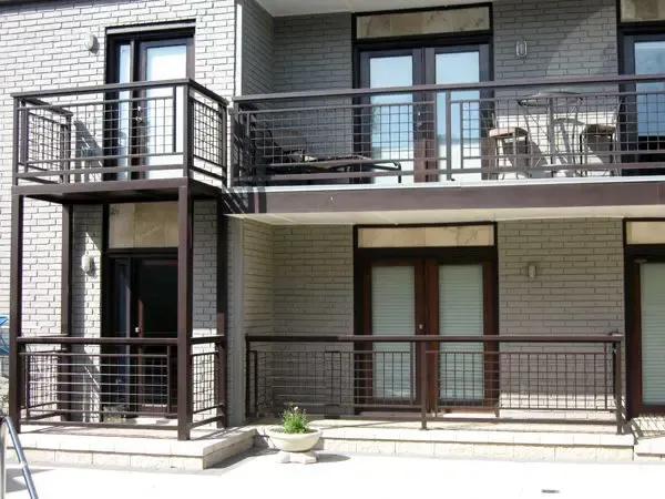 Two-story building with dark metal balconies and railings. Brick facade, glass doors and windows, outdoor seating.