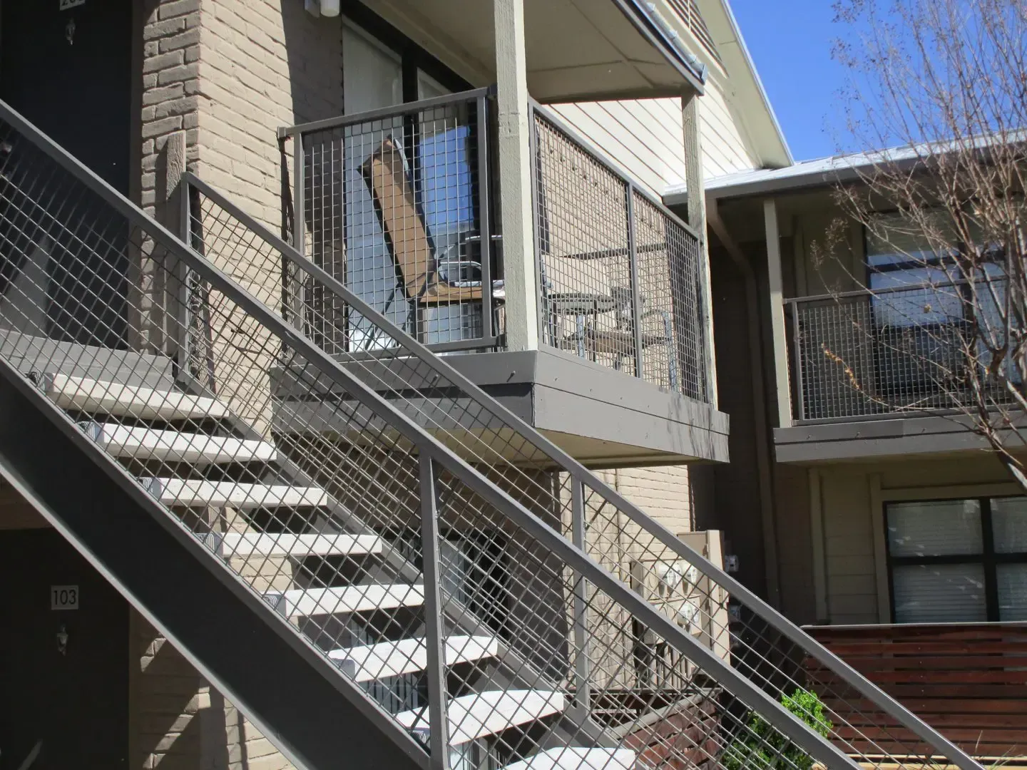 Outdoor apartment stairs with metal railings leading to a balcony with a chair.