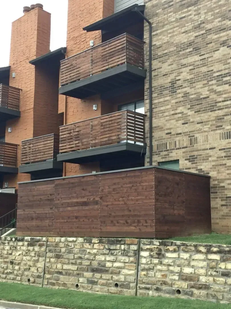 Apartment building exterior with brick and brown wood balconies and a retaining wall.