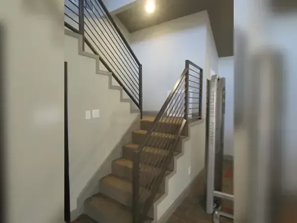 Staircase with metal handrails, carpeted steps, and gray walls.