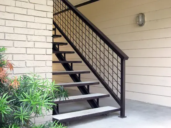 Exterior staircase with black metal railing, going up to a second story, beside a brick wall.