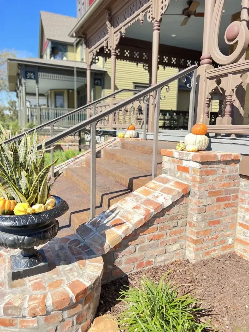 Brick steps leading up to a Victorian house with a railing and pumpkins.