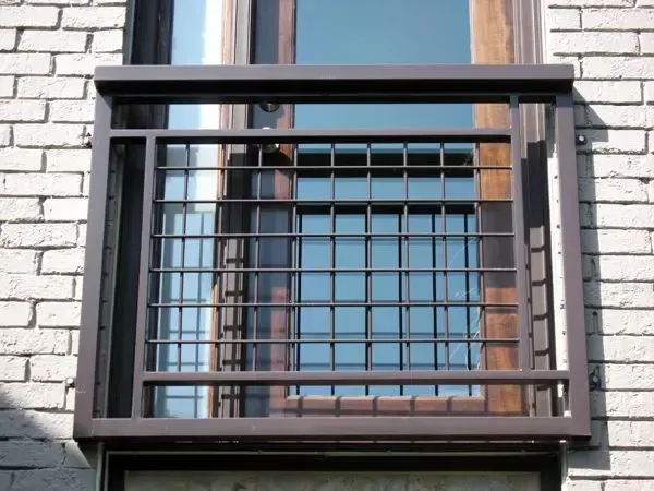 Brown metal window guard with a grid pattern on a brick building.