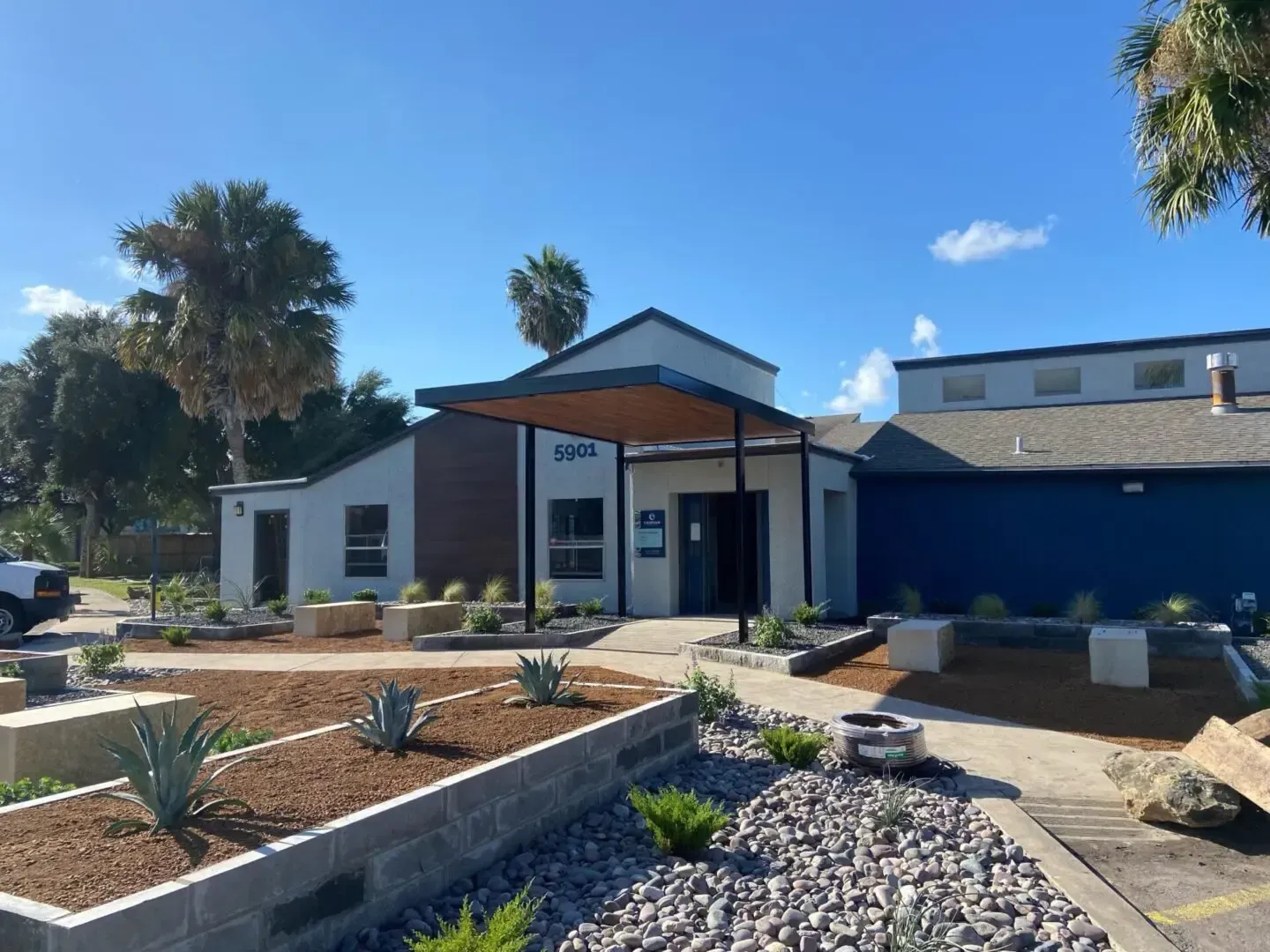 Exterior view of a modern building with blue accents, landscaping, and a clear sky.