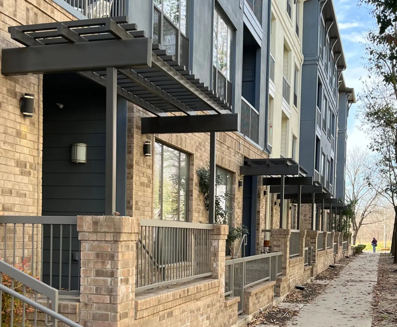 Row of townhouses with brick and gray facades, pergolas, and a sidewalk.
