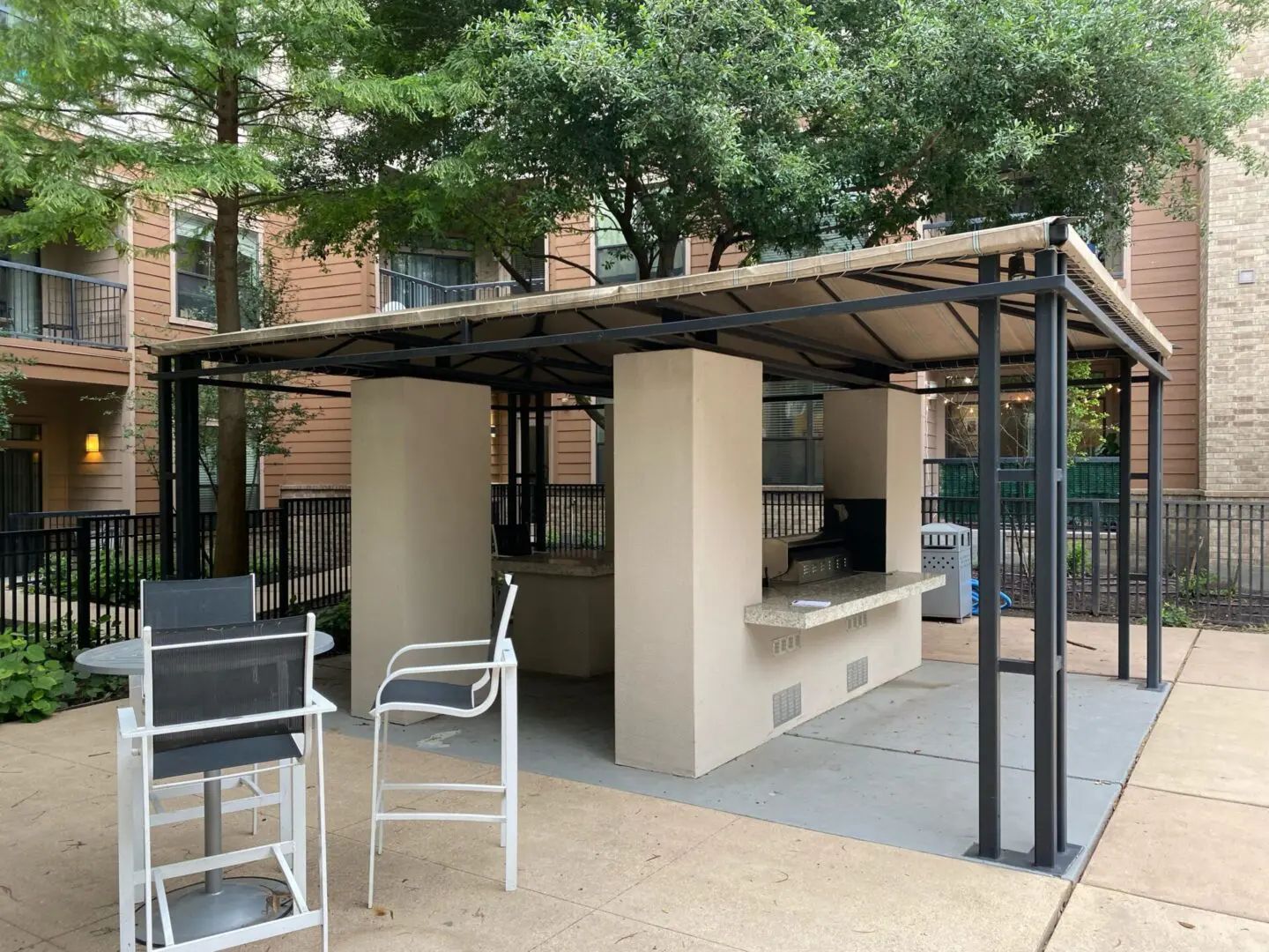 Outdoor grill area with tan structure, counters, and chairs.