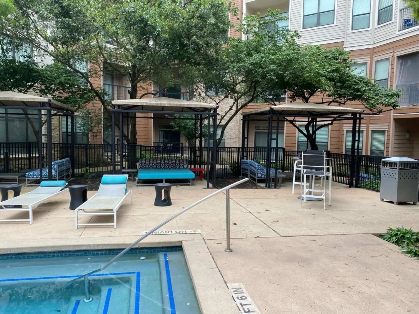 Poolside seating area with lounge chairs, cabanas, and a trash can.