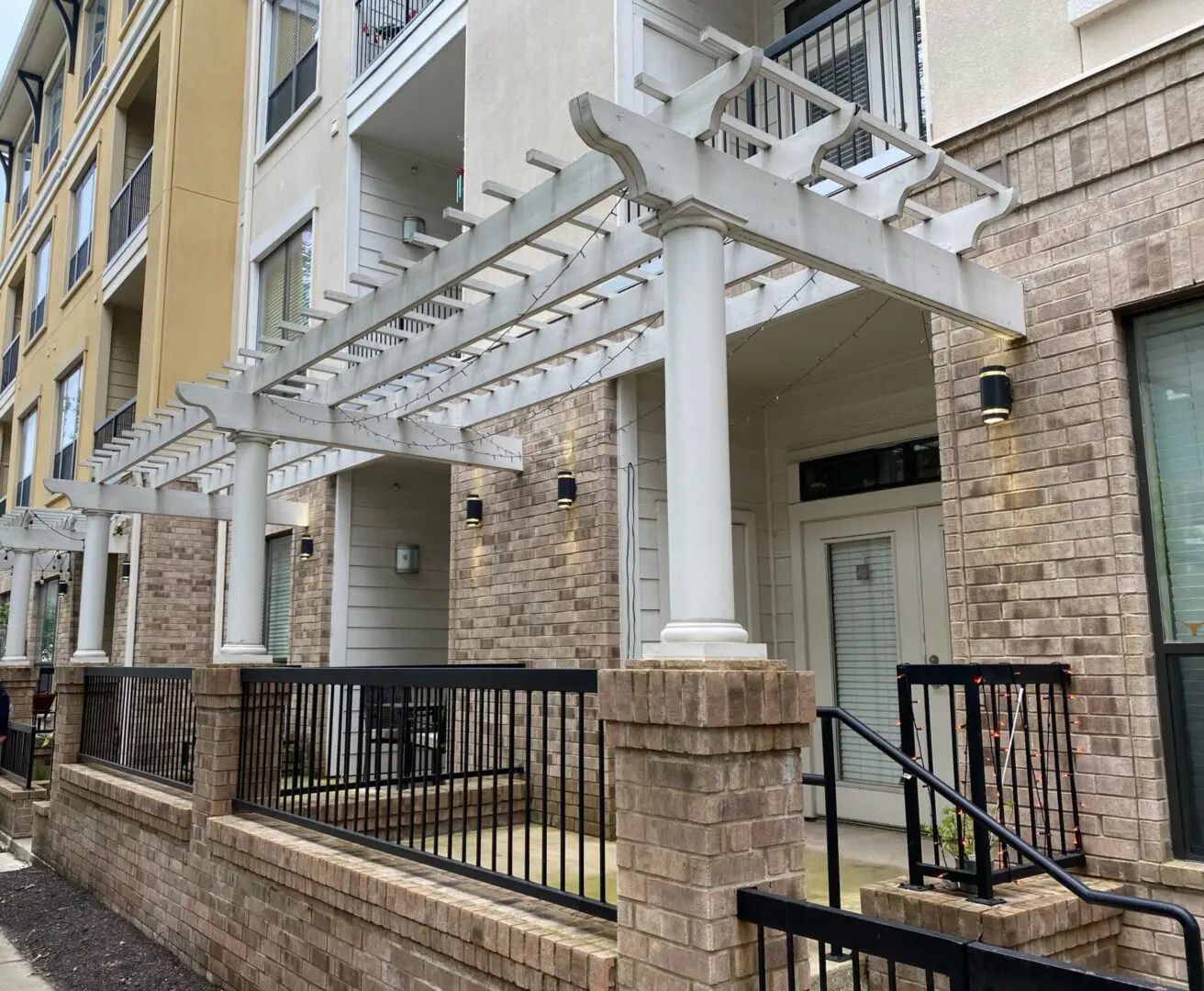 Apartment building exterior with a white pergola, brick accents, and black railings.