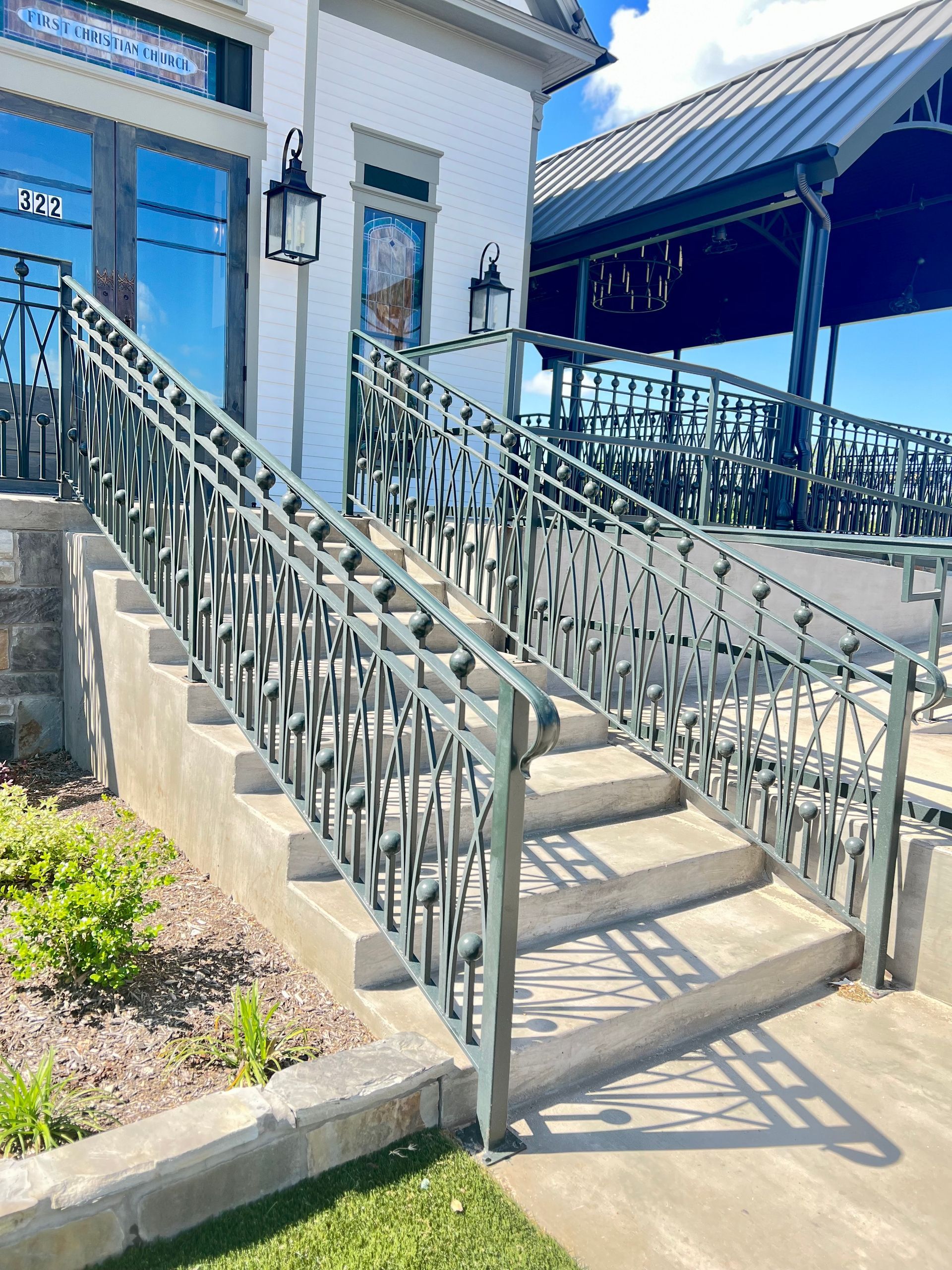 Outdoor concrete stairs with decorative metal railing leading to a building entrance with glass windows.
