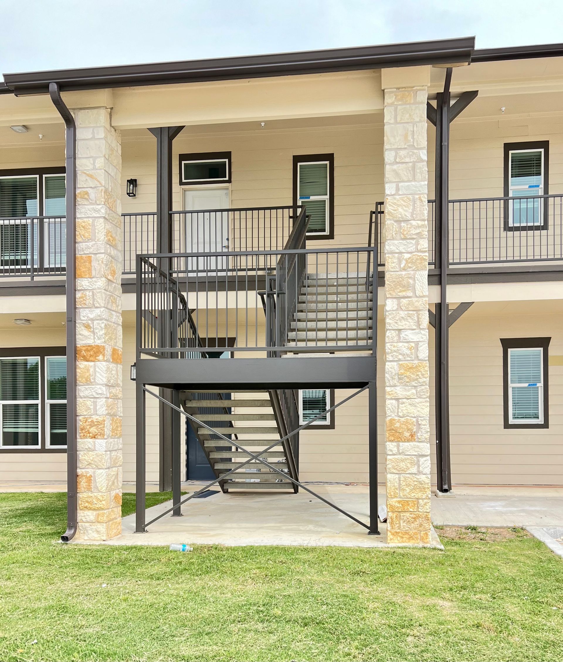 Two-story apartment building with exterior metal stairs, stone pillars, and light beige siding.