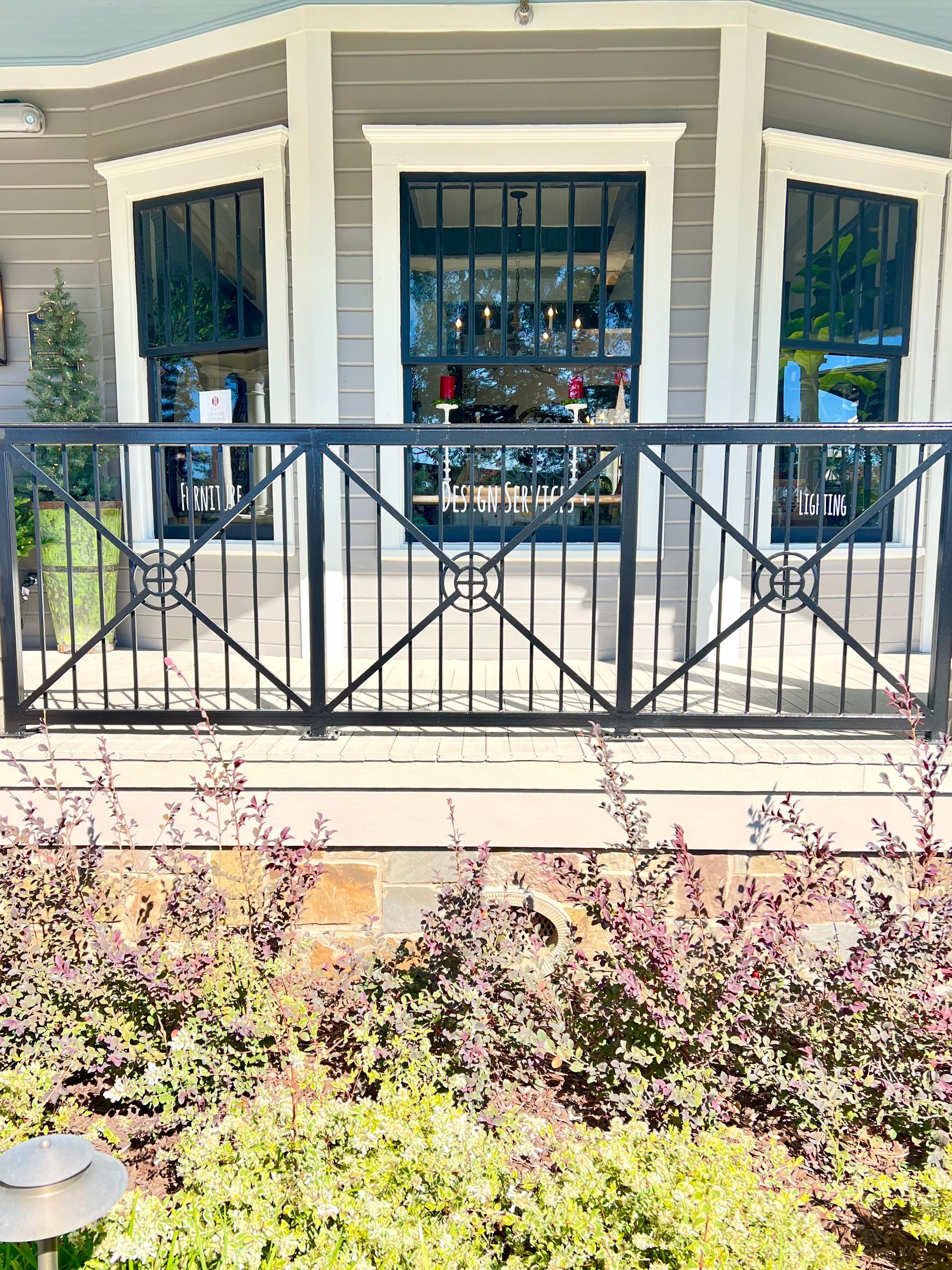 Black metal fence in front of a gray building with large windows. Green plants below.
