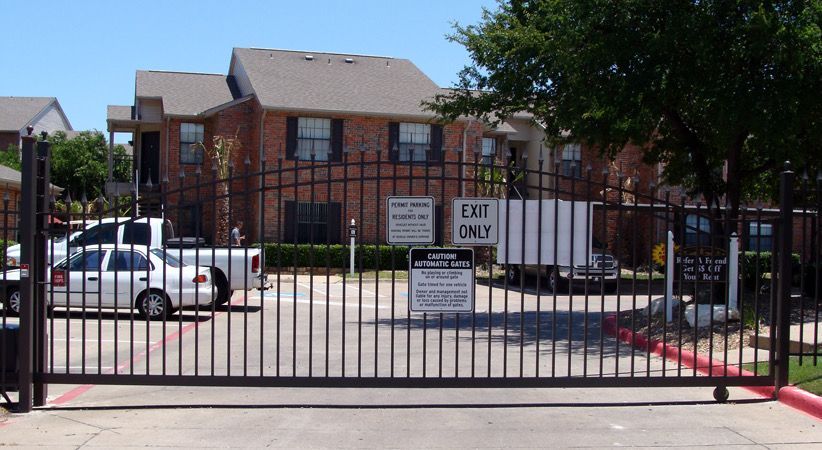 Black security gate in front of a brick apartment building with a white truck parked behind the gate.