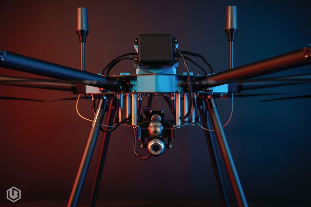 Front-facing drone with mounted camera and antennas against a blue-red gradient background