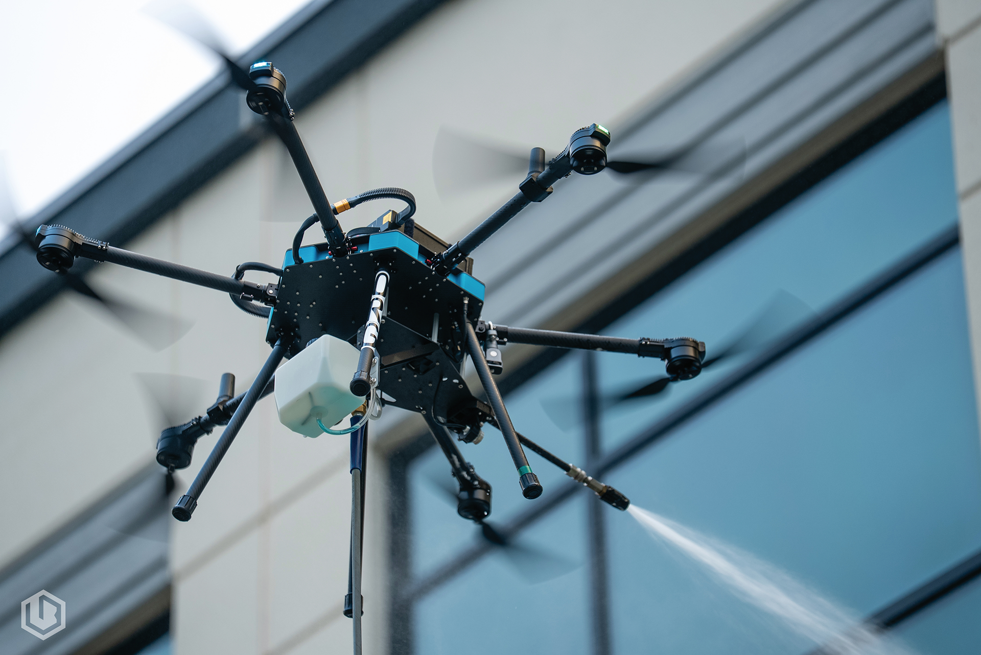 Close-up of a black drone with extended arms flying indoors against a glass building background