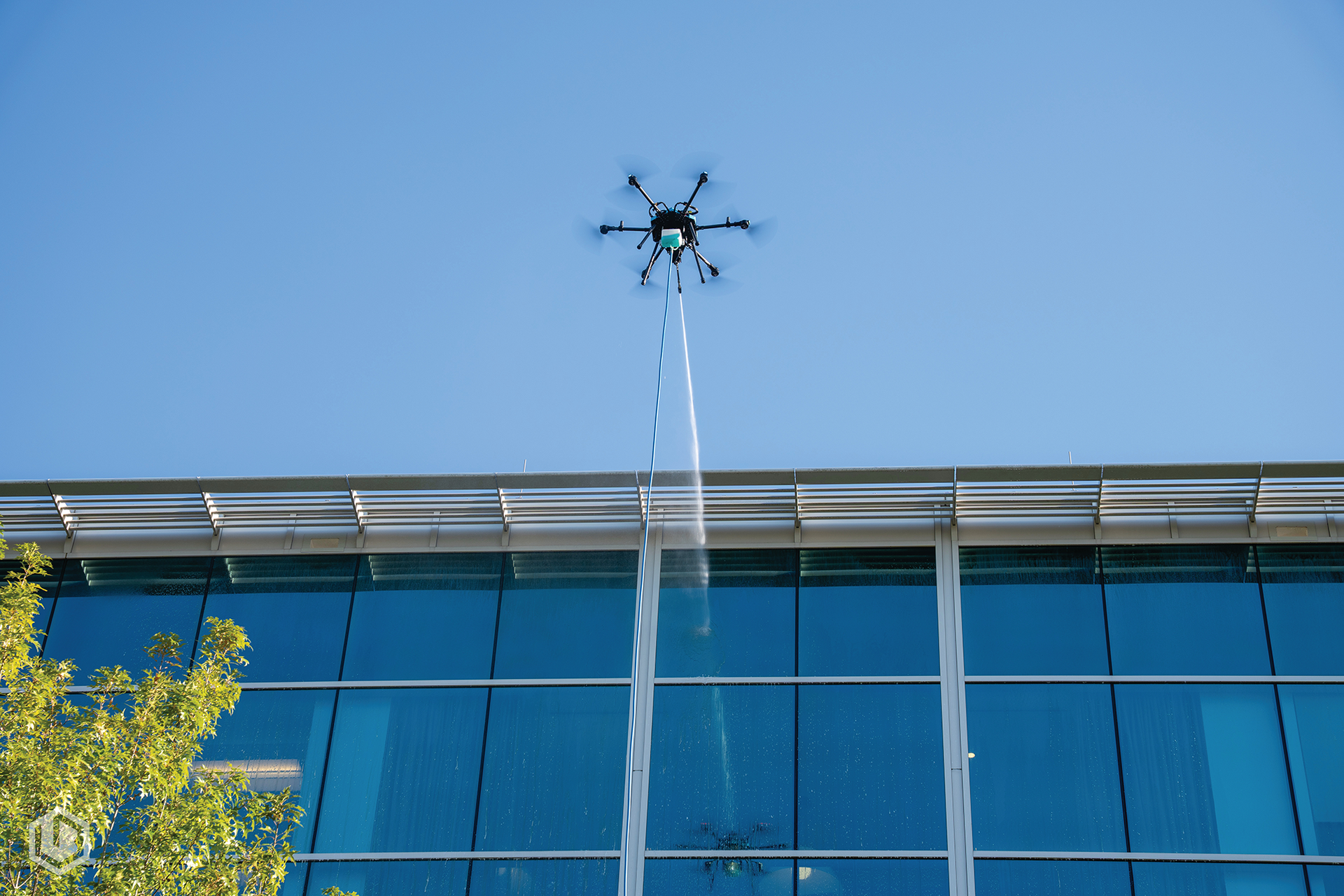 Drone flying above a blue-glass building against a clear sky