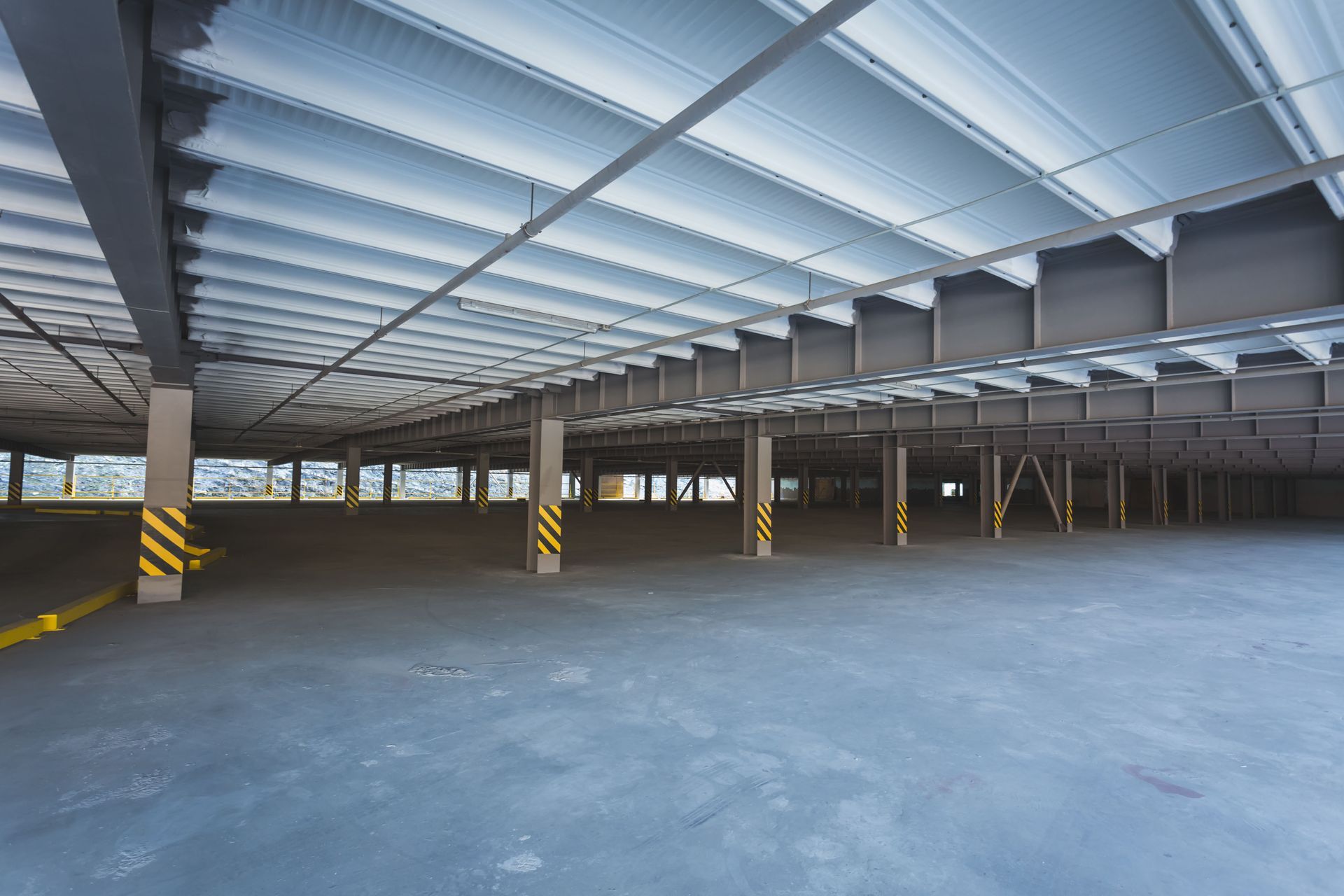 Empty industrial warehouse with a concrete floor, steel columns, and a translucent roof.
