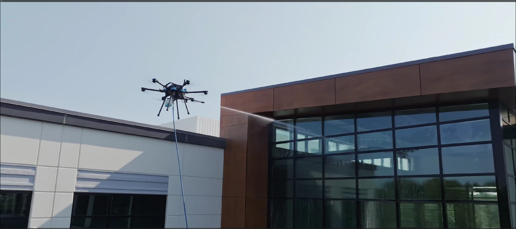 Drone flying above a modern building with large glass windows and a brown facade