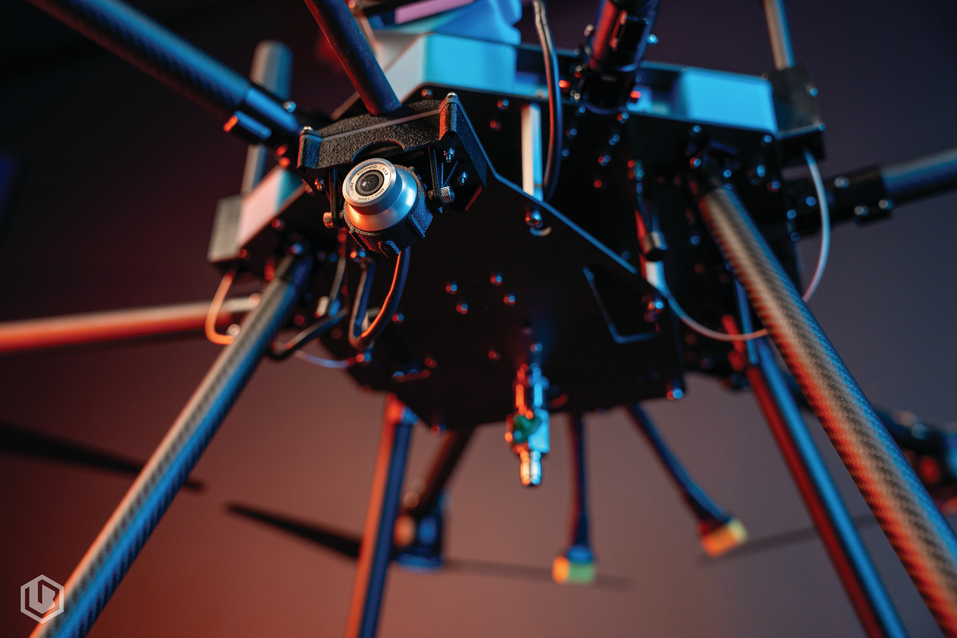 Close-up of a futuristic drone with glowing blue lights and carbon-fiber legs against a blurred red-blue background