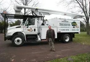 A man is standing in front of a tree service truck.