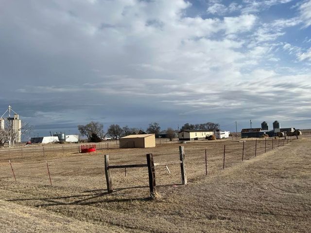 A fence surrounds a large dry grass field with buildings in the background.