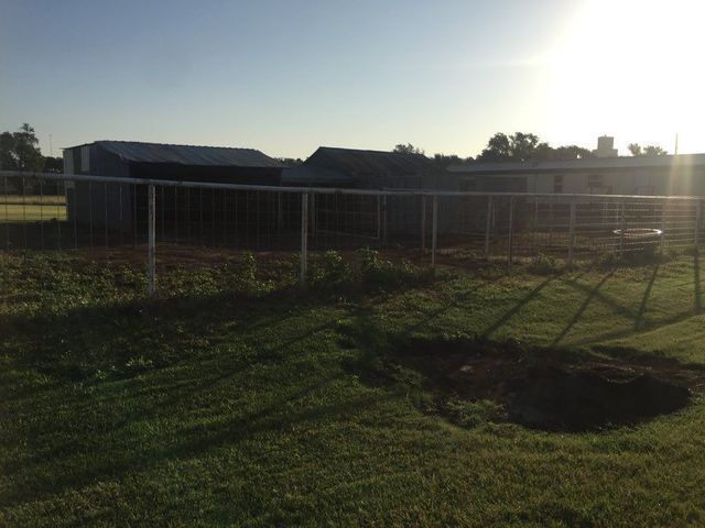 A fence surrounds a grassy field with a barn in the background.