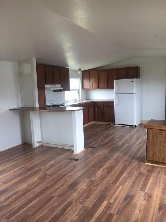 An empty kitchen with wooden floors and a refrigerator.