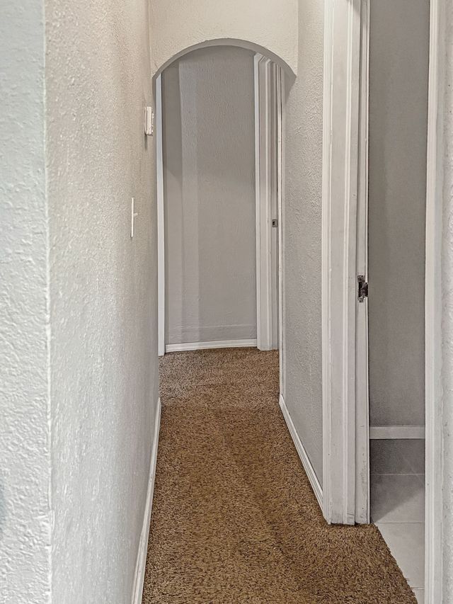 A long hallway with a brown carpet and white walls leading to a bathroom.