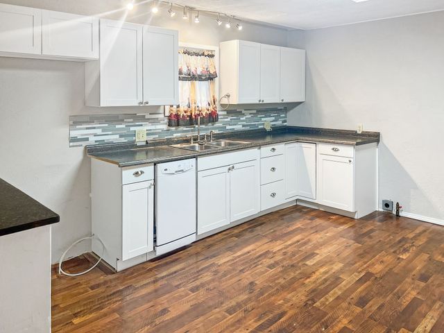 A kitchen with white cabinets and hardwood floors.
