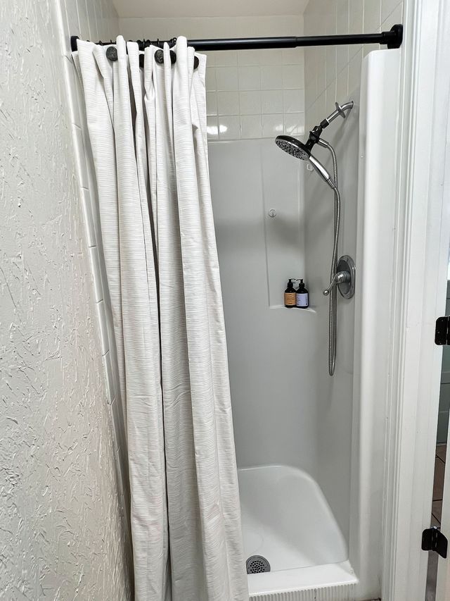 A shower with a white shower curtain and a shower head.