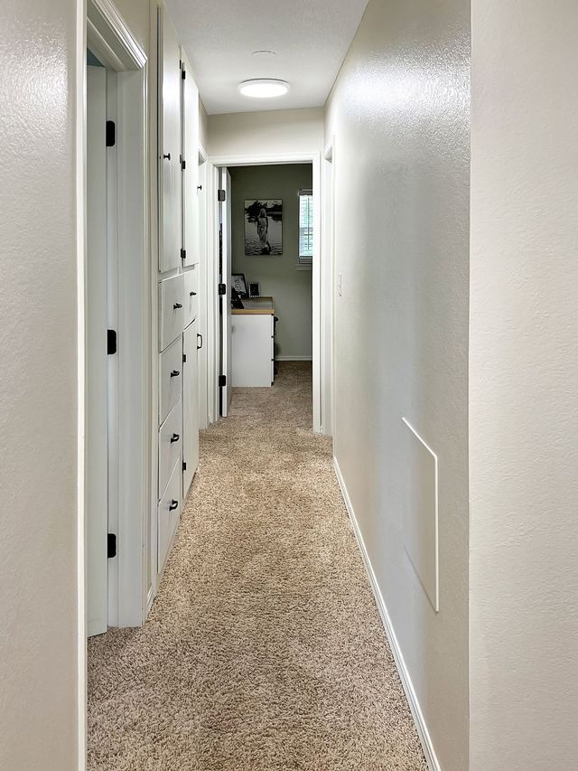 A long hallway in a house with a carpeted floor and white walls.