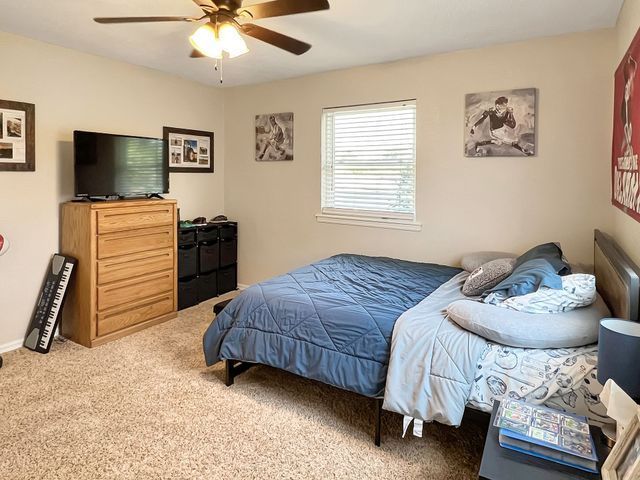 A bedroom with a bed , dresser , television and ceiling fan.