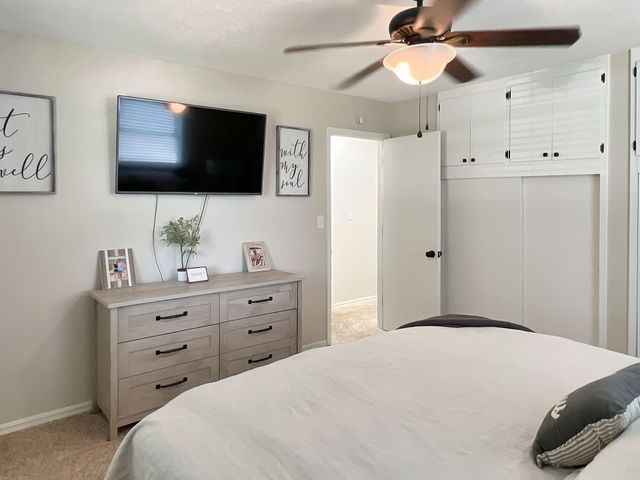 A bedroom with a bed , dresser , television and ceiling fan.