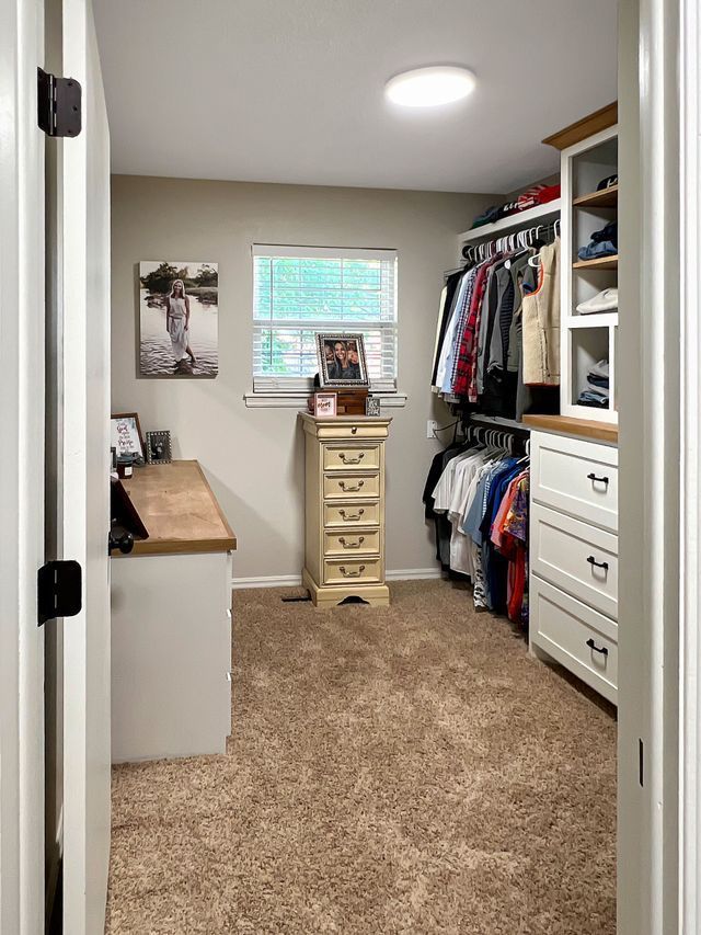 A walk in closet with a desk , dresser , drawers and a window.