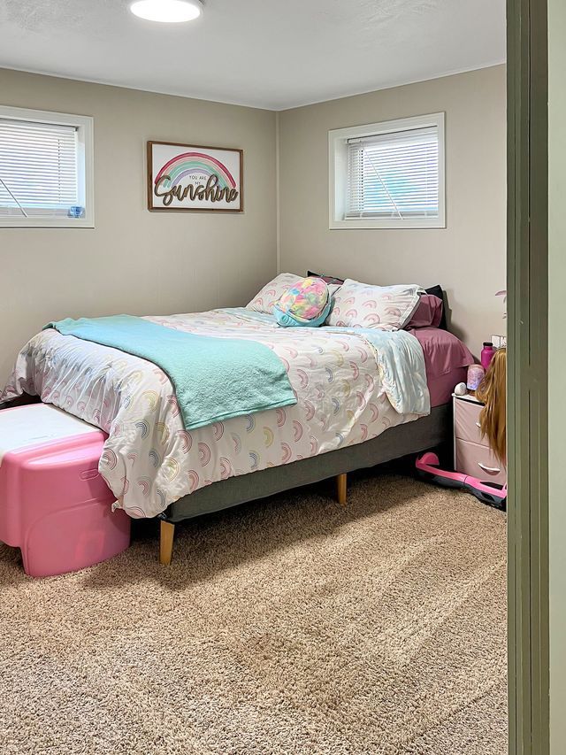 A bedroom with a bed , ottoman , and window.