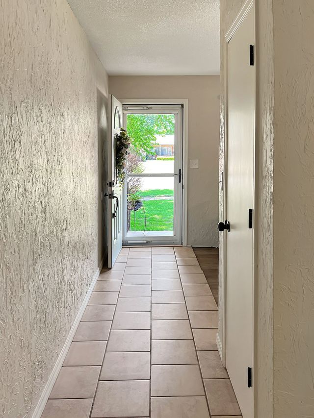 A hallway with tile floors and a glass door leading to the front door of a house.