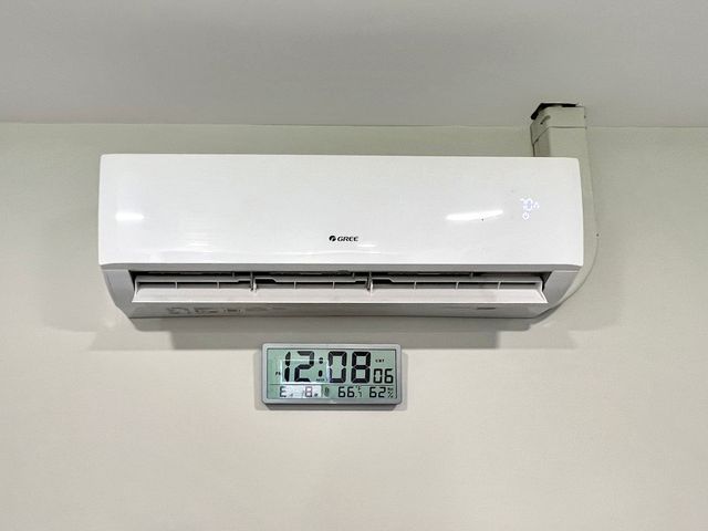 A white air conditioner is hanging on a wall next to a digital clock.