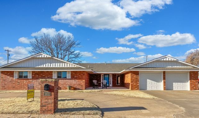 A brick house with two garages and a blue sky with clouds in the background.